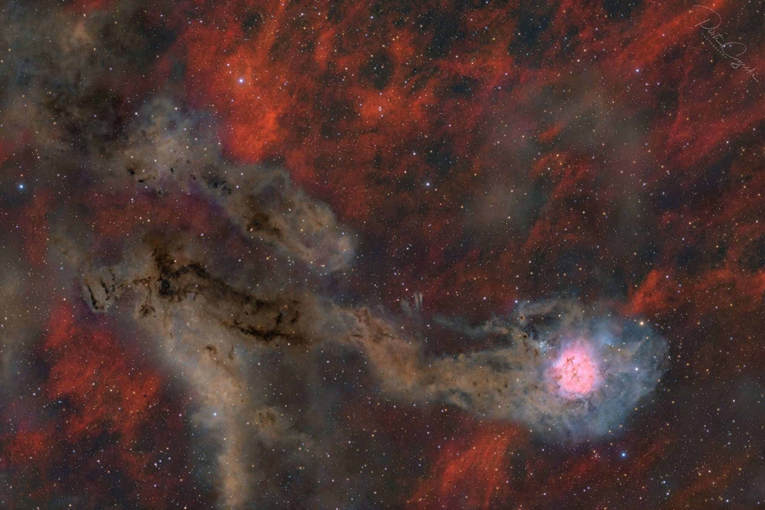 A starfield is shown against a patchy red-glowing
background. Two irregular brown trails occur, the lower
of which culminates in a bright pink and white region.
Please see the explanation for more detailed information.